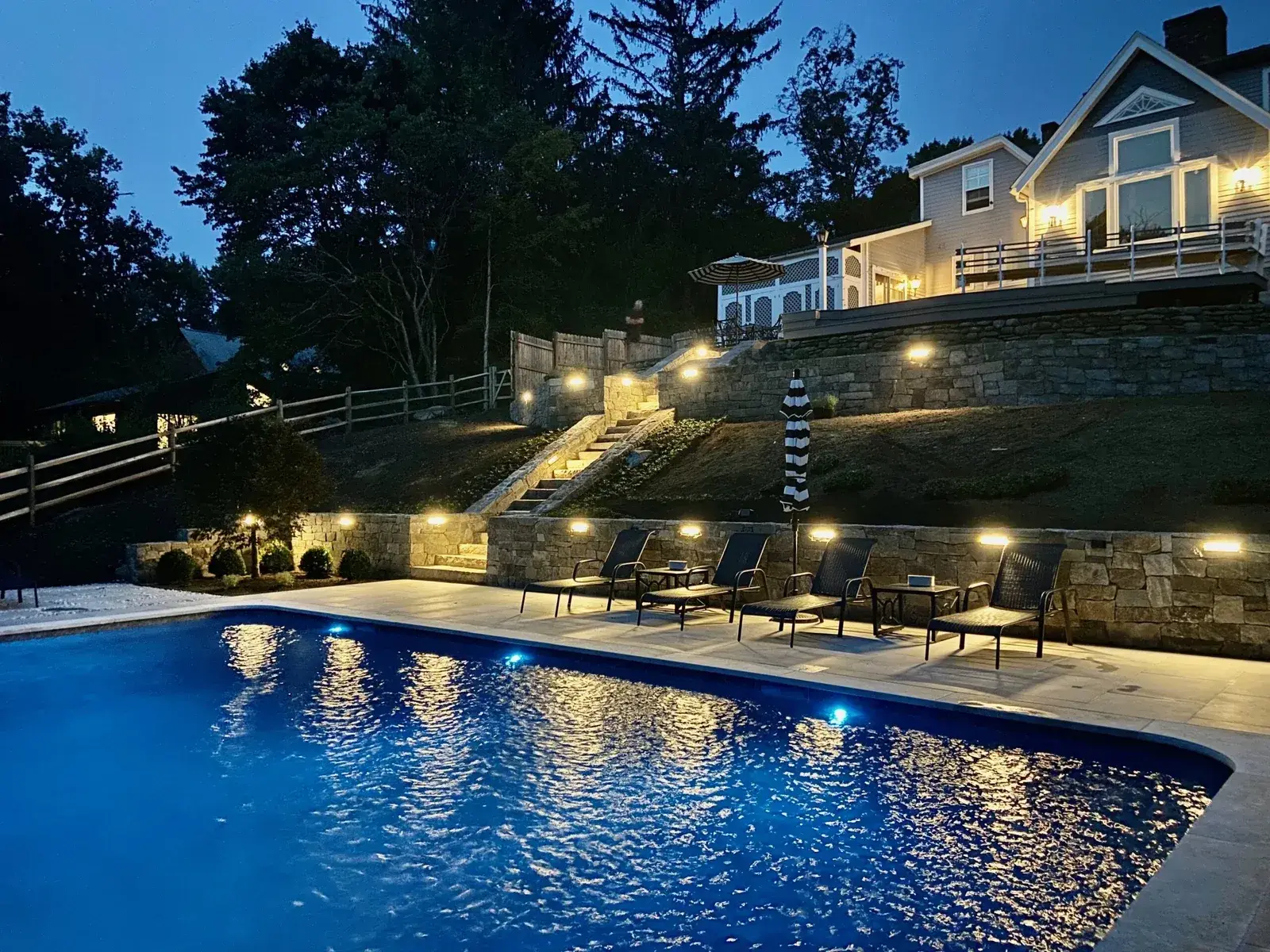 Pool with landscape lighting and stone walls at night in Fairfield County, CT by Creative Minds Landscaping